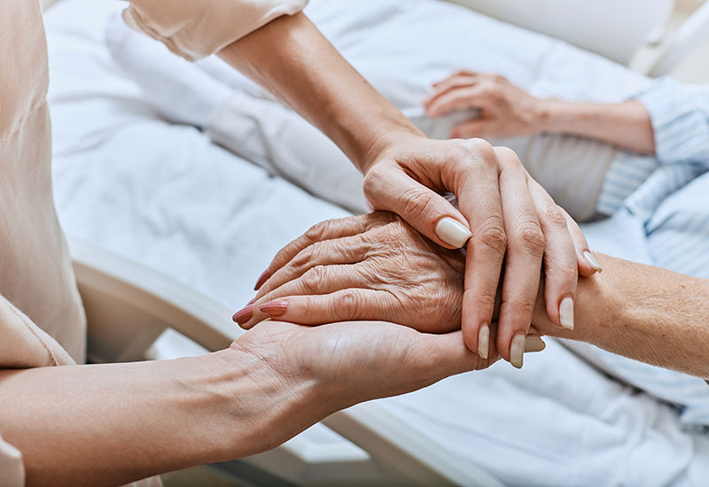 Woman holds the hand of a relative in hospice care at Alpine Skilled Nursing & Rehabilitation in Ruston, LA